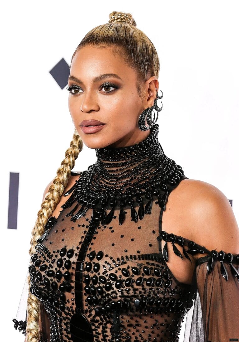 Beyoncé: Wears a sheer black dress adorned with beads and sparkling details that highlight her…