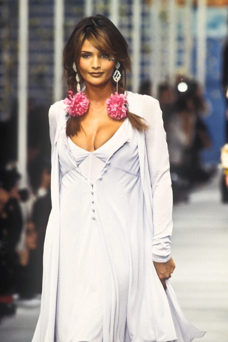 Helena Christensen: Wears a long lavender dress with a deep neckline and front buttons…