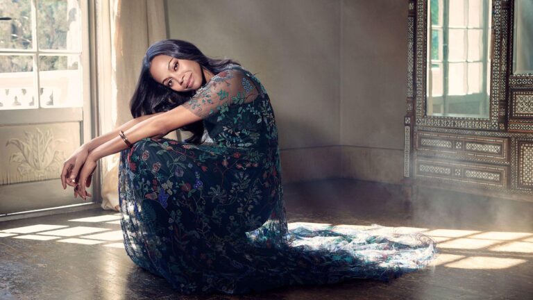Zoe Saldaña: Dressed in a long, semi-sheer gown with an intricate floral design in dark tones,…