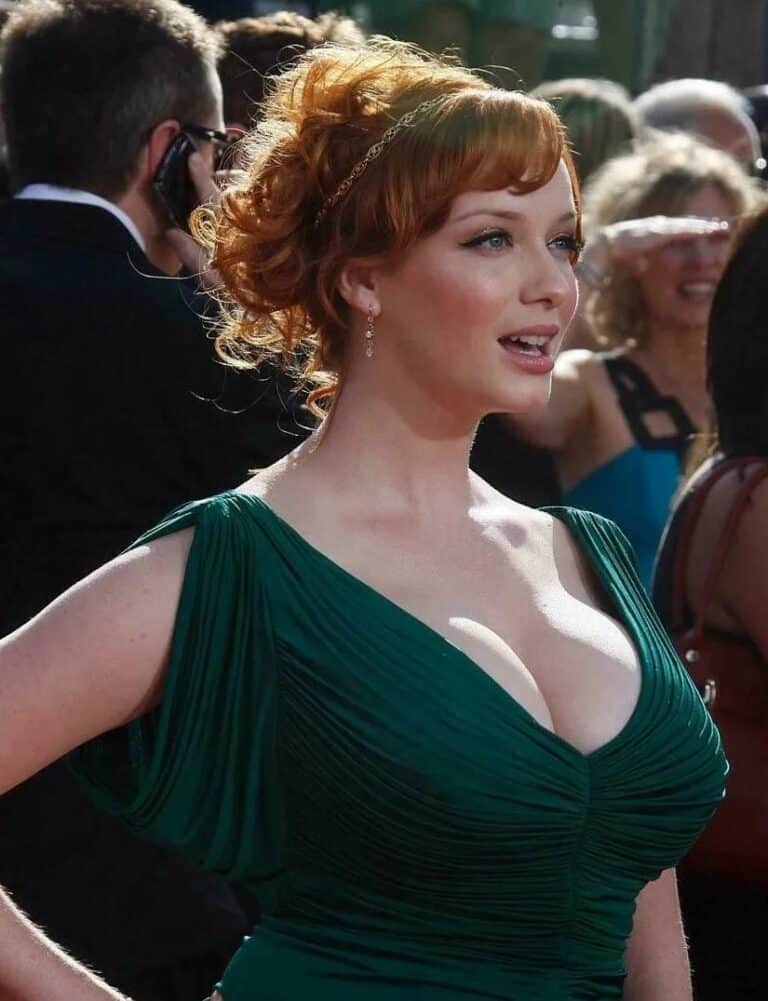 Christina Hendricks: Wearing a green pleated dress with a V-neck. Her hair is pulled back…