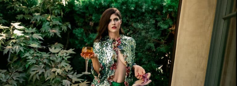 Alexandra Daddario: Wears a green sequined jacket and a striking floral necklace. Holds a pair of…