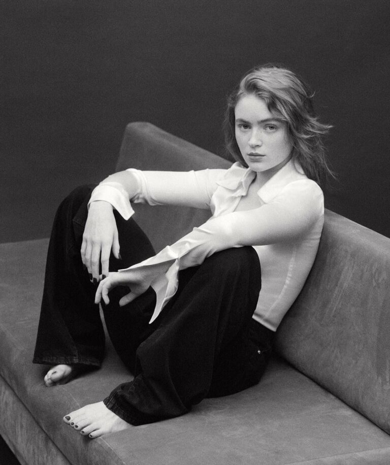 Sadie Sink: Wearing a white shirt with sleeve details and dark pants. Has no…