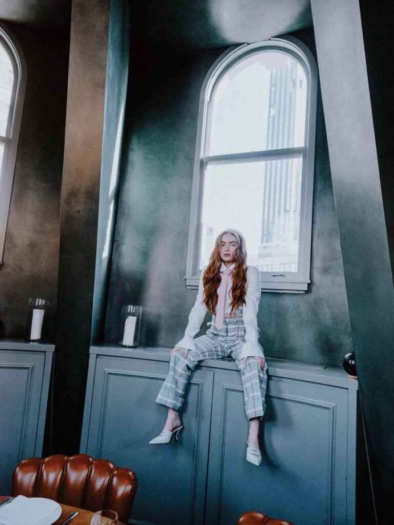 Sadie Sink: Wearing white heeled shoes. The outfit includes a white shirt with a tie…