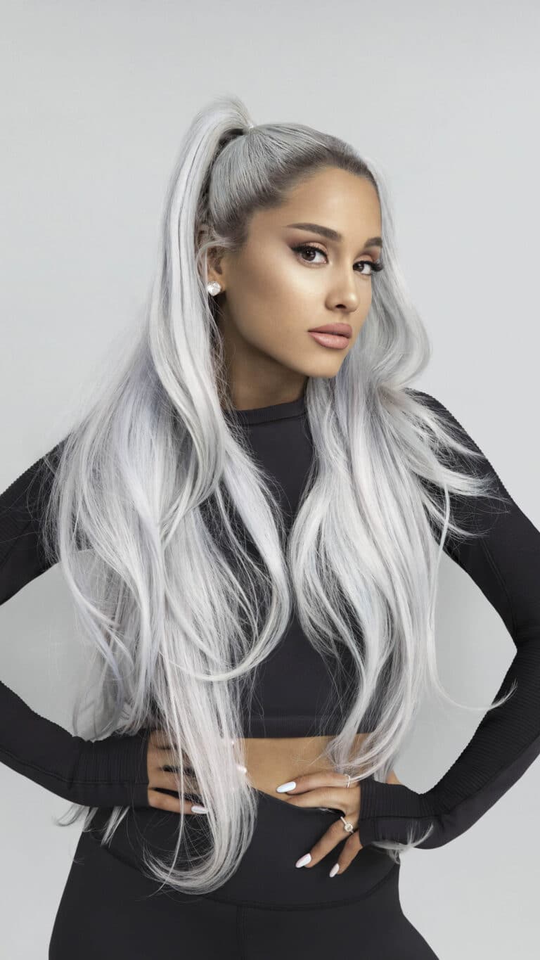 Ariana Grande: Cabello largo y plateado peinado en una coleta alta. Lleva una blusa negra de…