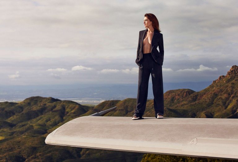 Anne Hathaway: Dressed in an elegant black suit, the figure stands on an airplane wing.…