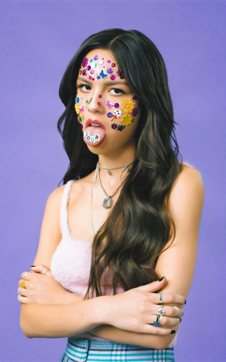 Olivia Rodrigo: Cabello largo y suelto, adornado con pegatinas coloridas en la cara. Luce un top…