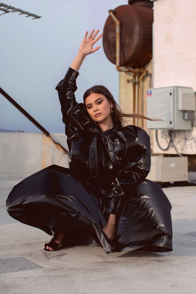 Lukita Maxwell: Viste un abrigo largo de material brillante en color negro. Lleva sandalias negras. Tiene…