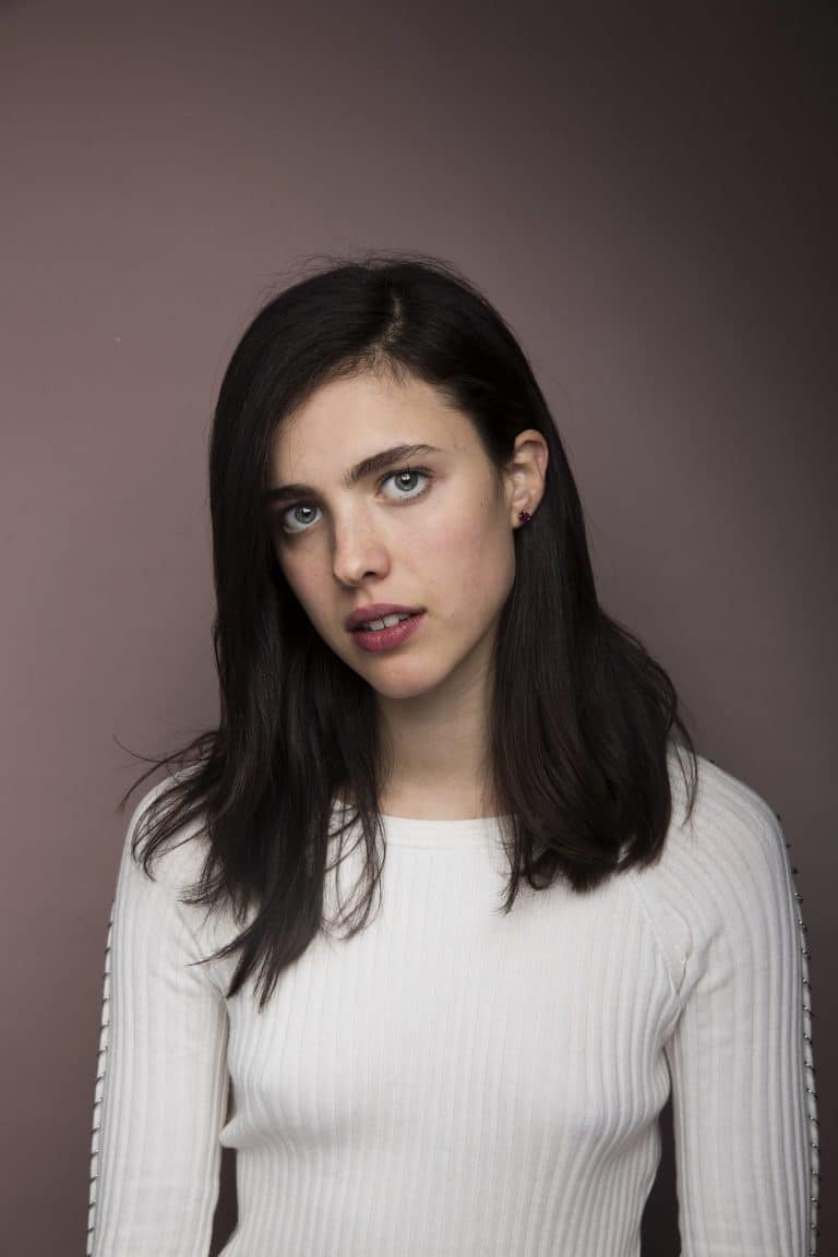 Margaret Qualley: El cabello es oscuro y lacio. La prenda es una camiseta blanca de manga…