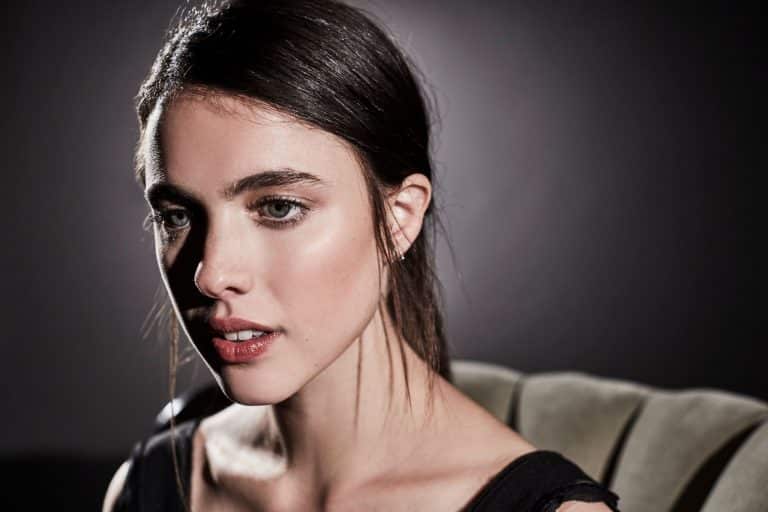Margaret Qualley: Lleva una camiseta negra de tirantes. El cabello está peinado hacia atrás. No se…