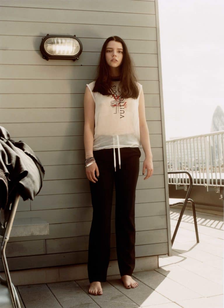 Anya Taylor-Joy: No shoes visible. Wears a white sleeveless tee with a lettered design and…