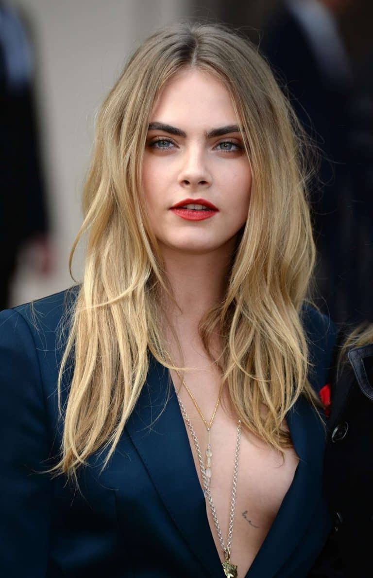 Cara Delevingne: Lleva el cabello largo y suelto. Viste un blazer azul oscuro con un escote…