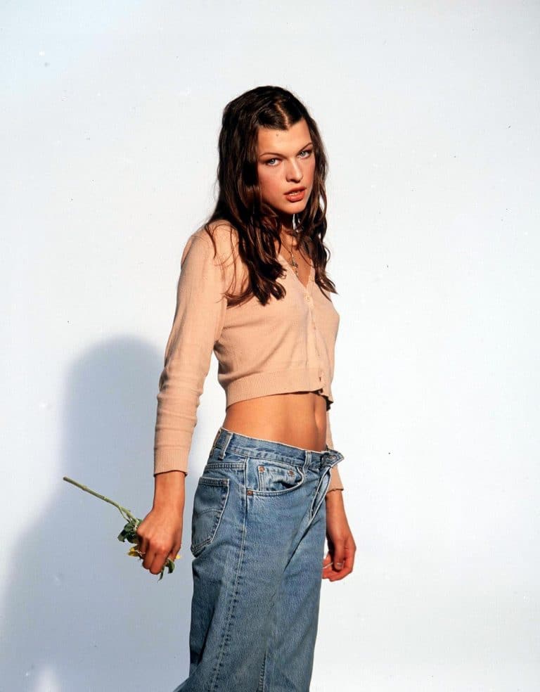 Milla Jovovich: Wears a short, buttoned beige cardigan with low-rise, slightly loose jeans.…