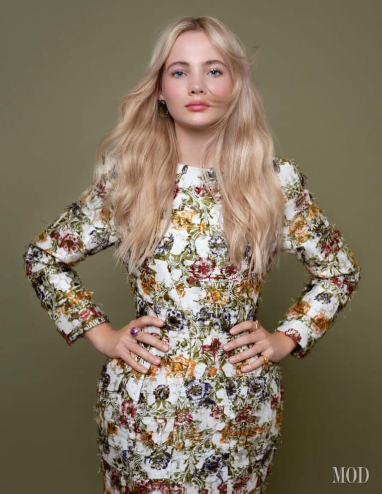 Freya Allan: Wears a long-sleeved floral dress in green, orange and purple tones. The…