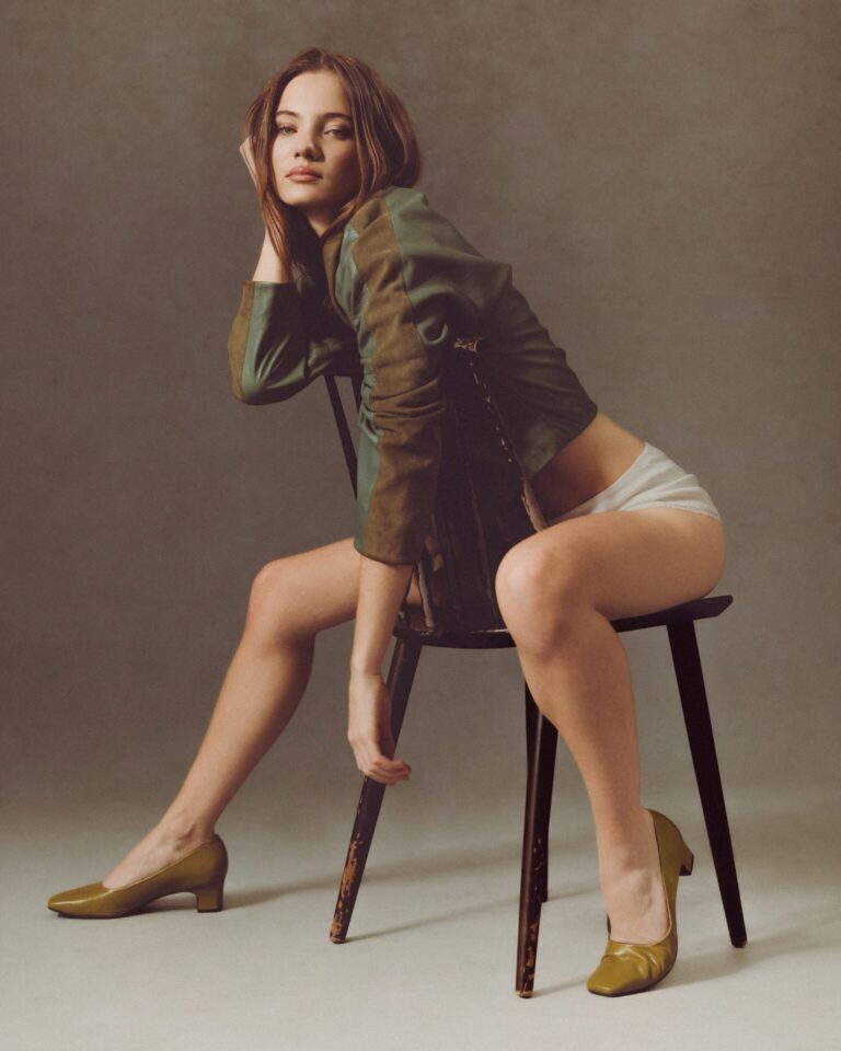 Freya Allan: Green jacket with brown details, worn over white underwear. The footwear is…