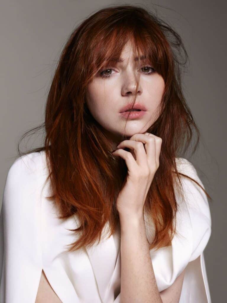 Karen Gillan: Long red hair worn loose, with bangs falling over the forehead. Wears a…