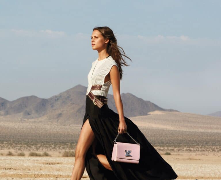 Alicia Vikander: Wears a dress with a black skirt featuring a large slit and a white blouse…