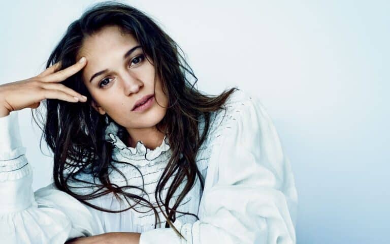 Alicia Vikander: Wears a white blouse with pleated details and wide sleeves. Her hair is long…