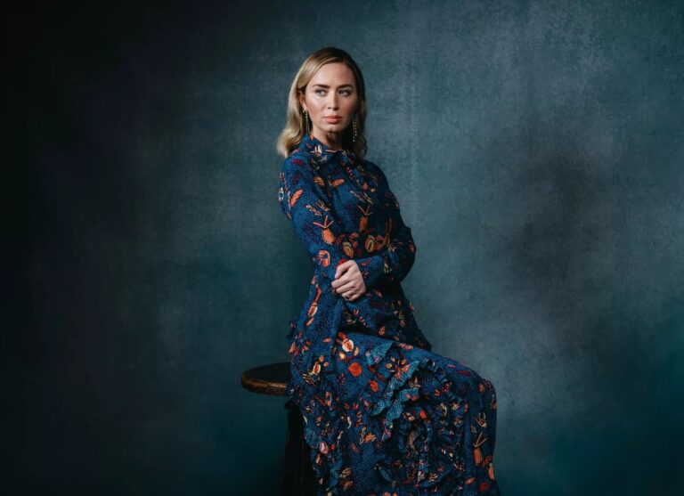 Emily Blunt: Wearing a long blue dress with a floral print in orange and red tones, of…