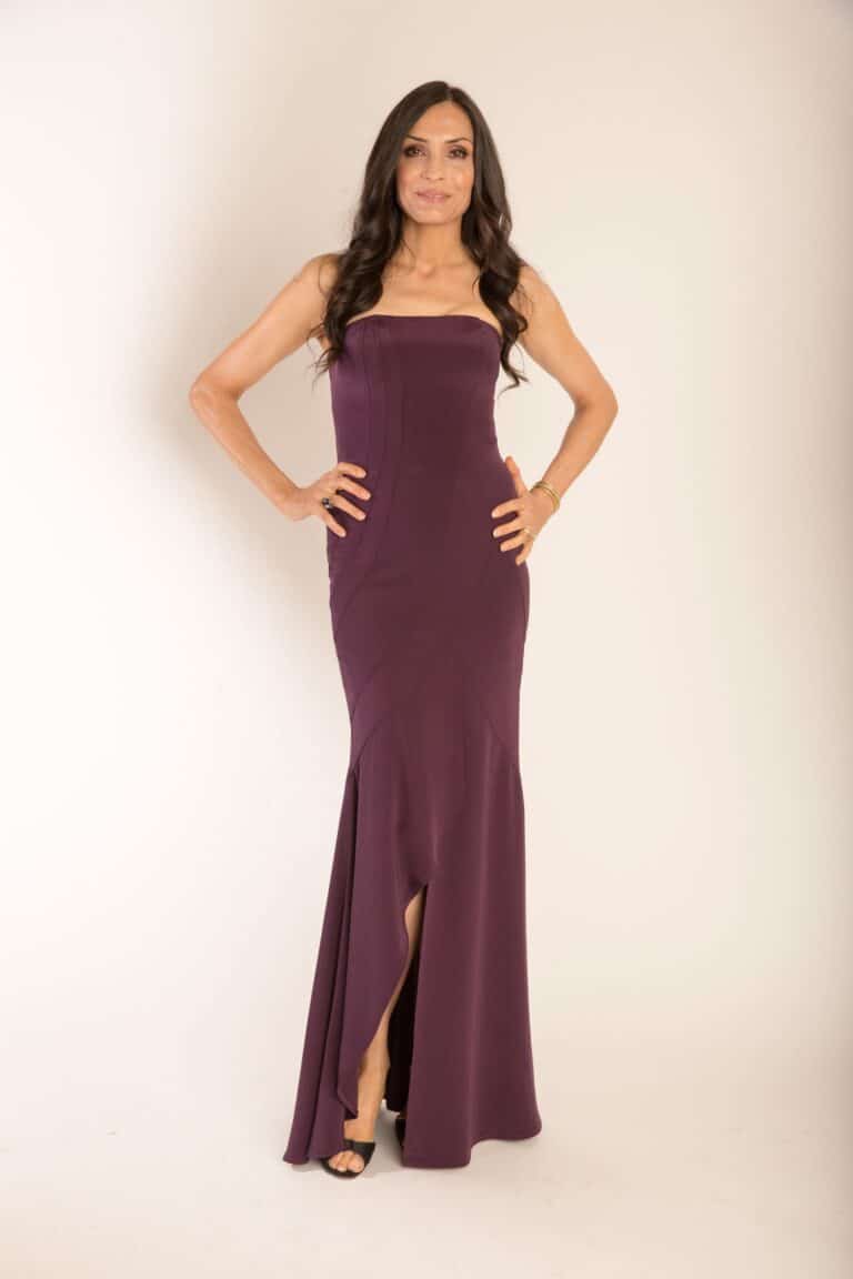 Famke Janssen: Long purple dress with a fitted design and a front slit. Wearing…