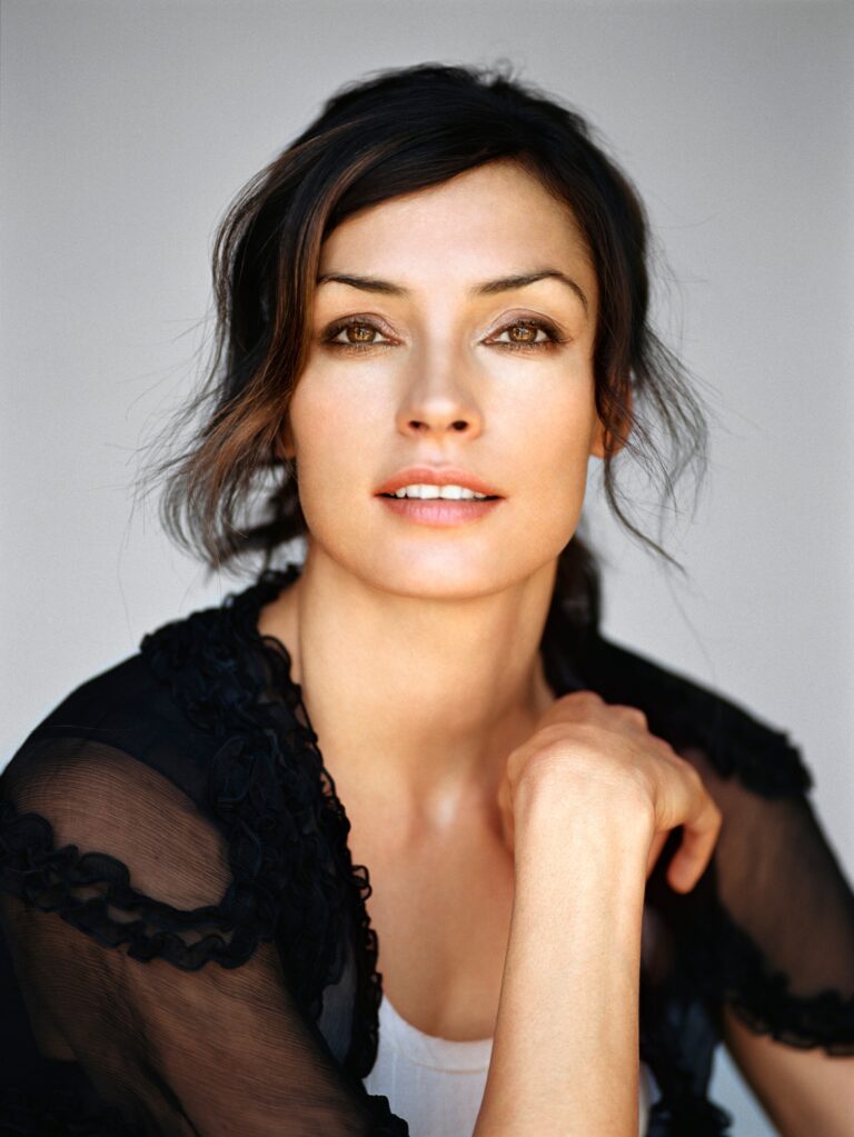 Famke Janssen: The setting is simple, with a neutral background that highlights the central image. The…