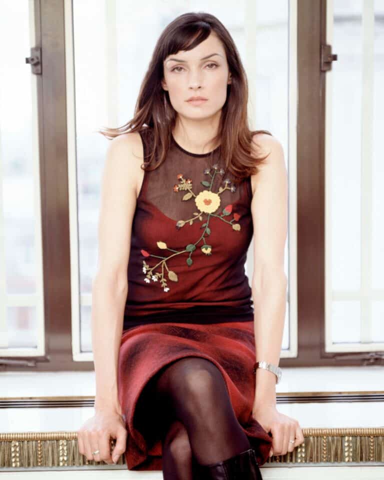 Famke Janssen: Wears a dark sleeveless dress with embroidered floral details, paired with…