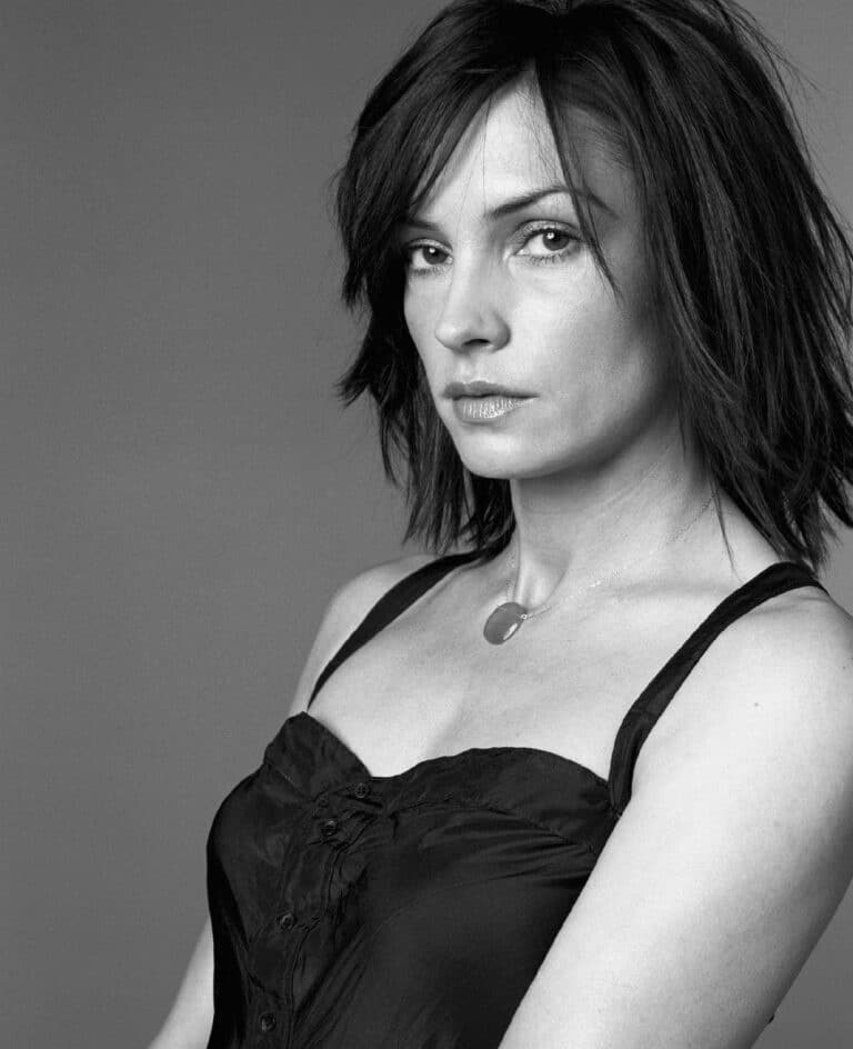 Famke Janssen: Dark hair worn loose, with a serious expression. Wears a black top with straps…