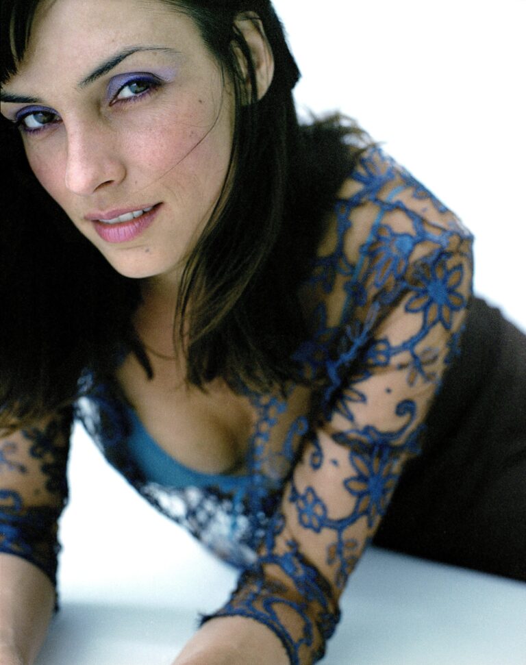 Famke Janssen: Wearing a blue lace blouse with floral details over blue lingerie.…