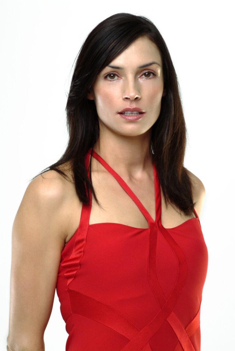 Famke Janssen: Wears a red dress with crisscross straps, no visible accessories. Her hair is straight…