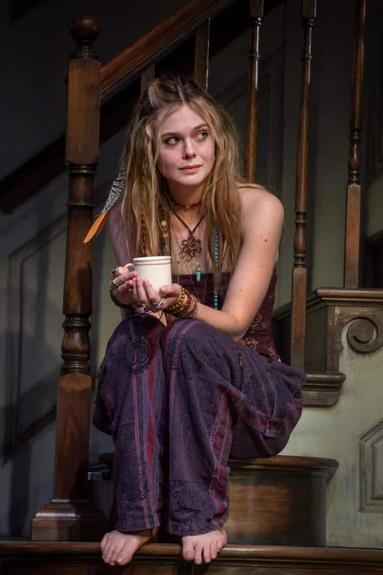 Elle Fanning: Sitting on a wooden staircase, wearing a dark sleeveless top and pants…