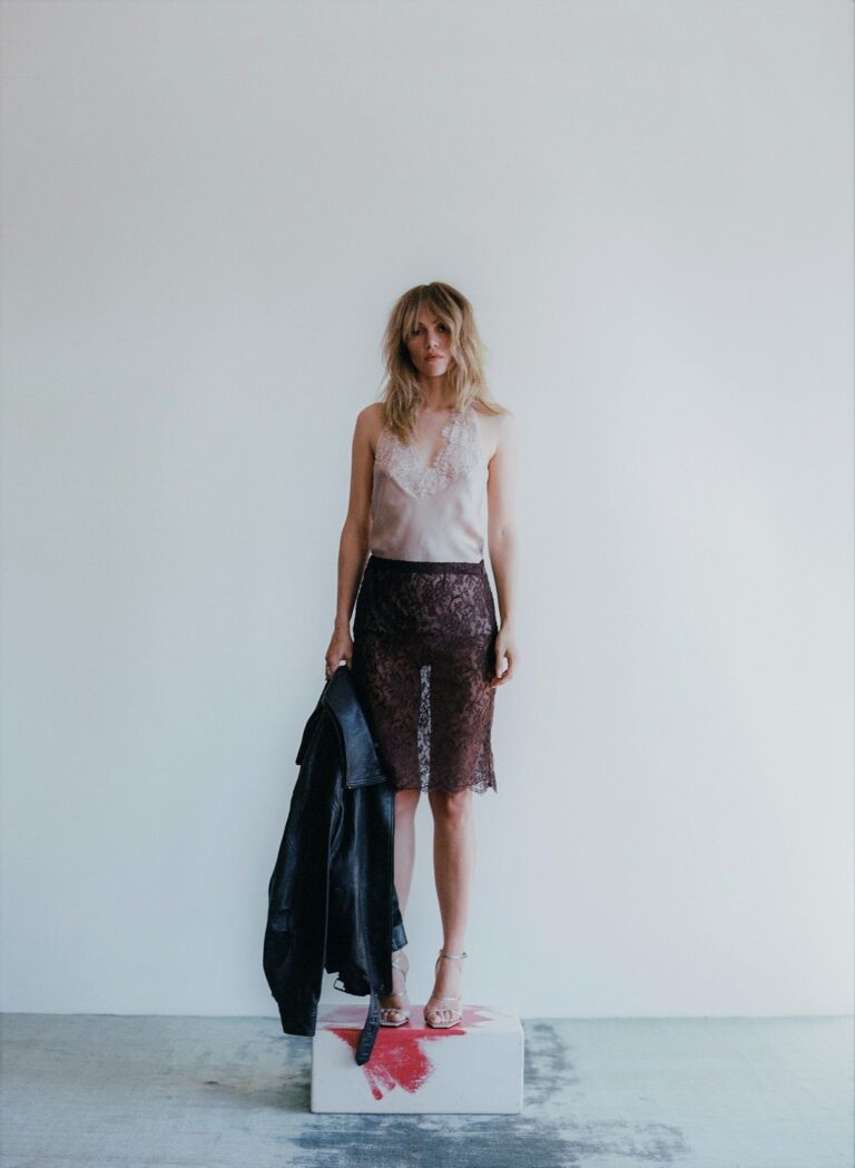 Suki Waterhouse: Luce una blusa clara con encaje y una falda de encaje negra. Sostiene una…
