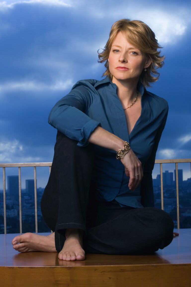 Jodie Foster: Blue shirt, dark pants and no shoes. Wears a gold bracelet and a necklace…