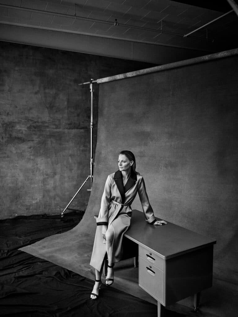 Jodie Foster: Wearing a long coat with dark details on the collar and sleeves, she is standing…