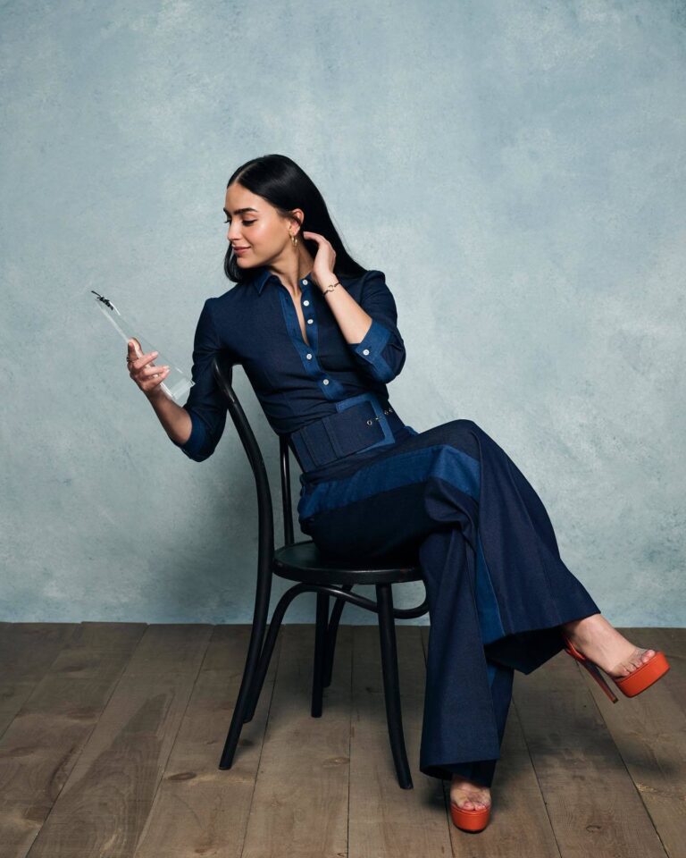 Melissa Barrera: Sitting on a wooden chair against a pale blue wall…