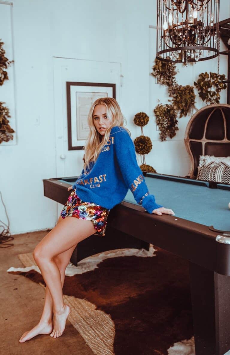 Madison Iseman: Wears a blue sweater with gold text and bright sequined shorts in several…