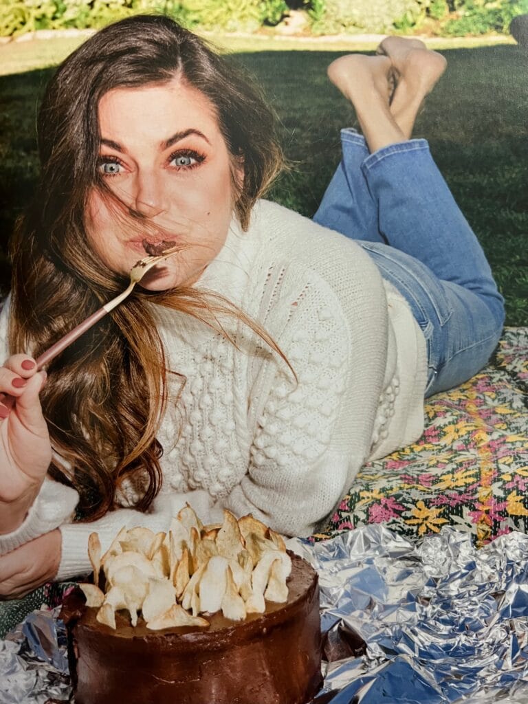 Tiffani Thiessen: Lleva un suéter blanco de punto y jeans azules, está descalza y se encuentra…