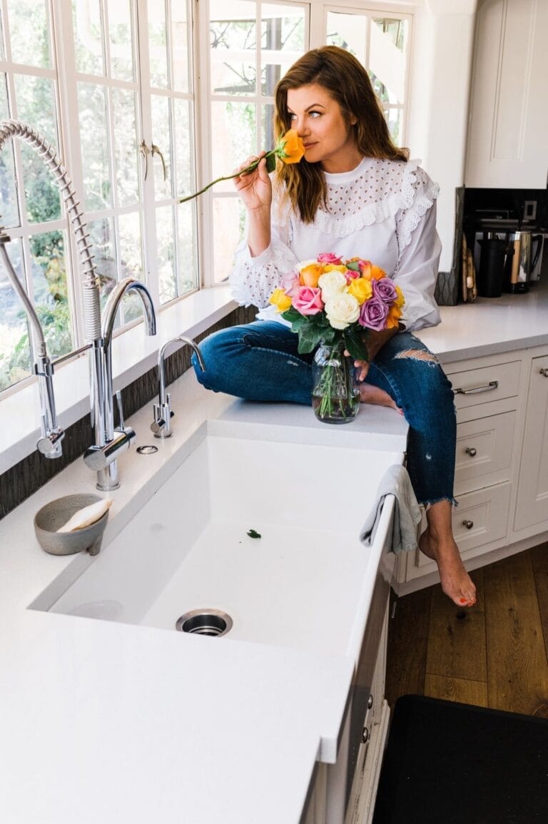 Tiffani Thiessen: Luce un blusa blanca de encaje y jeans rotos en la rodilla. Está descalza,…