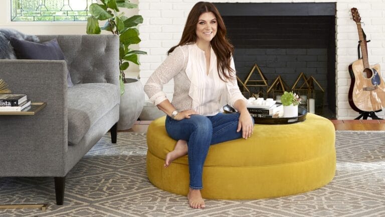 Tiffani Thiessen: Sentada en un puff amarillo, lleva una blusa clara con detalles de volantes y…