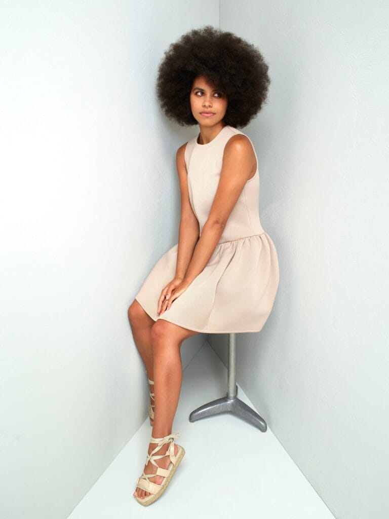 Zazie Beetz: Wears a sleeveless beige dress with subtle texture, paired with wedge sandals…