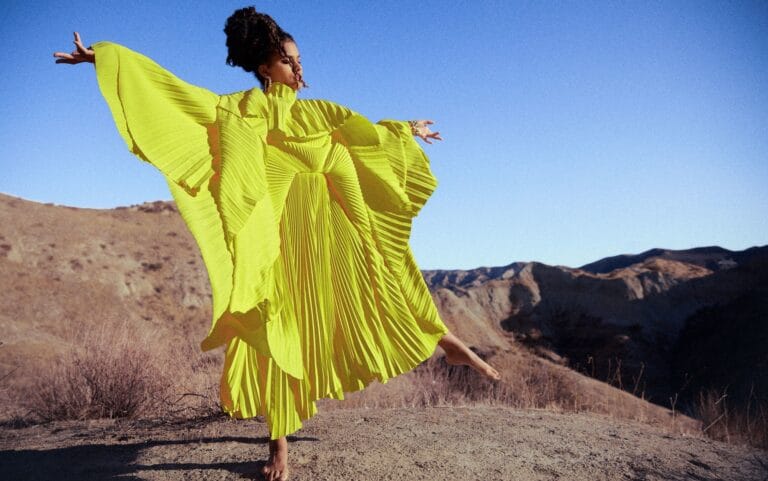 Zazie Beetz: Wears a bright yellow dress with wide, elegant pleats. No footwear is visible.…