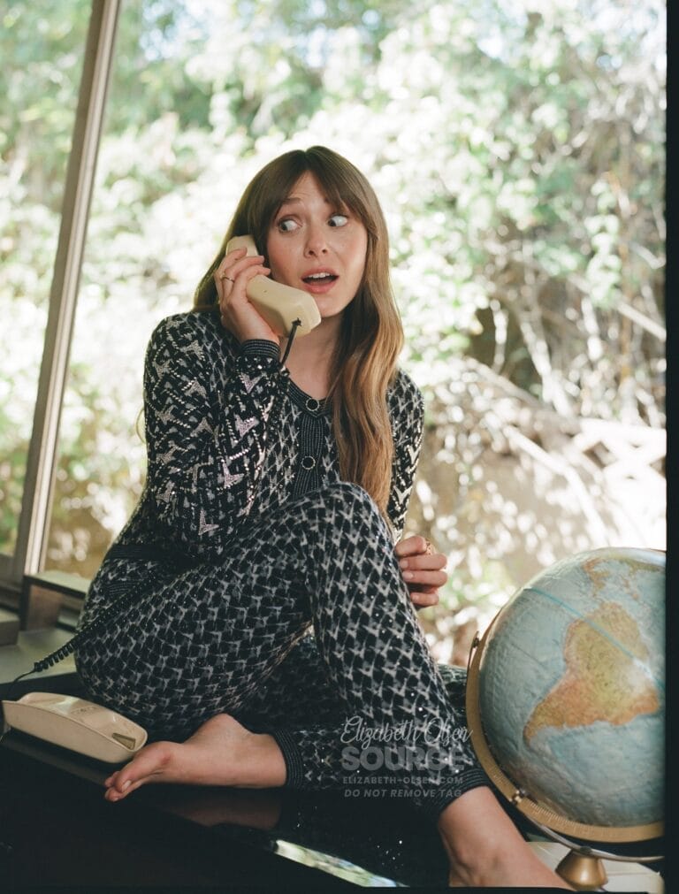 Elizabeth Olsen: Wears a black and white printed outfit. Is barefoot and holds a…