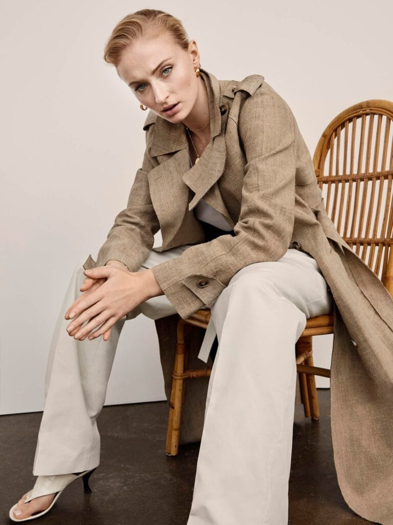 Sophie Turner: Wore a long beige coat over a white T-shirt and wide pants in a light tone, paired with…