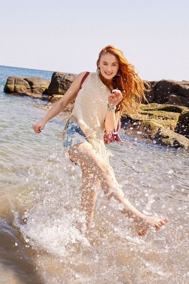 Sophie Turner: Wears a beige knit blouse and denim shorts. Carrying a pink backpack and…