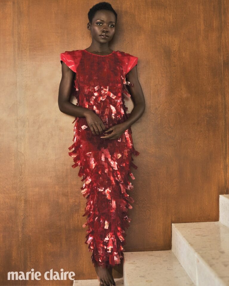 Lupita Nyong’o: Luce un vestido rojo brillante con adornos que parecen flecos, sin calzado visible. Está…