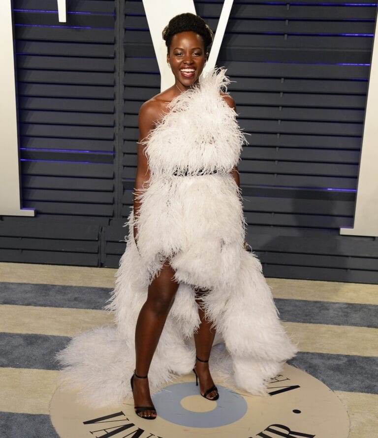 Lupita Nyong’o: Luce un vestido asimétrico de plumas blancas que destaca por su elegancia. Complementa con…