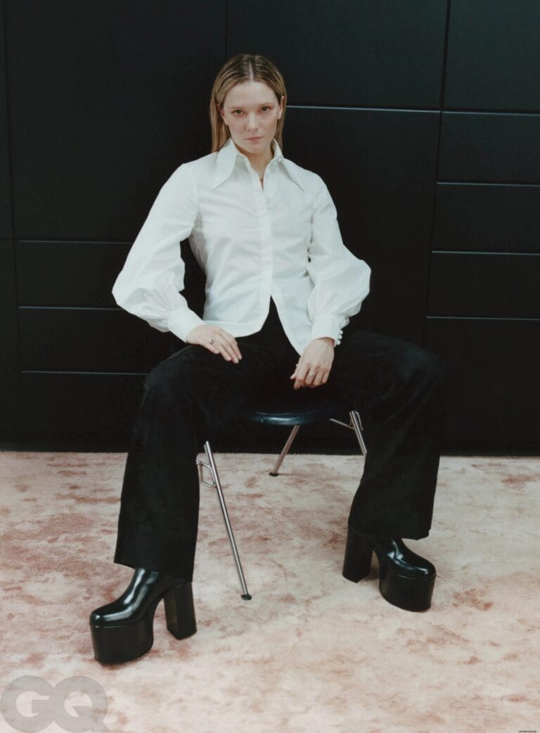 Morfydd Clark: Lleva una camisa blanca de mangas largas y pantalones oscuros acampanados. Calza zapatos de…