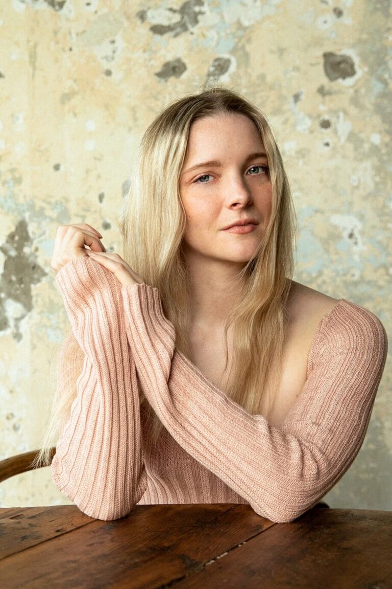 Morfydd Clark: Luce un suéter de punto en tono rosa claro, con hombros descubiertos. El cabello…