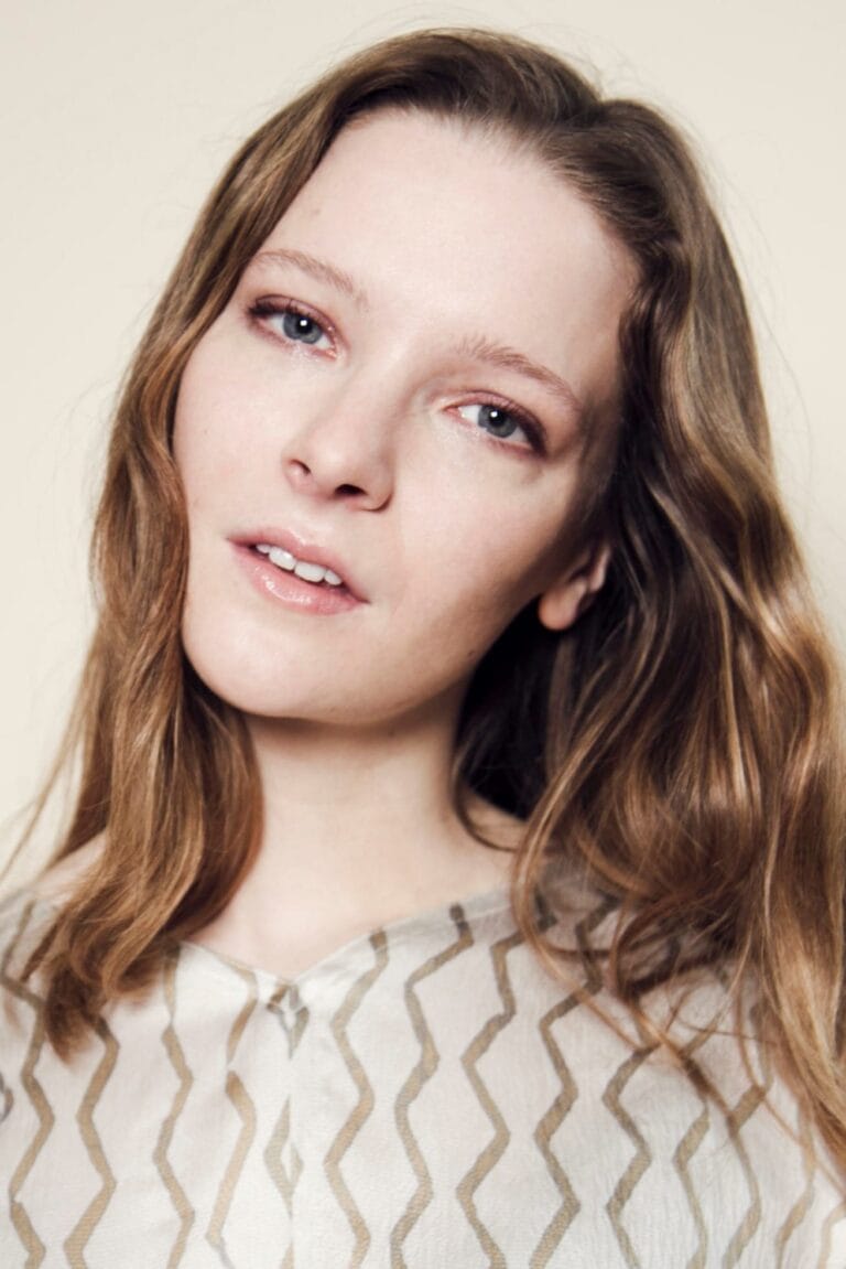 Morfydd Clark: Luce una camisa blanca con un patrón de líneas doradas en zigzag. El cabello…