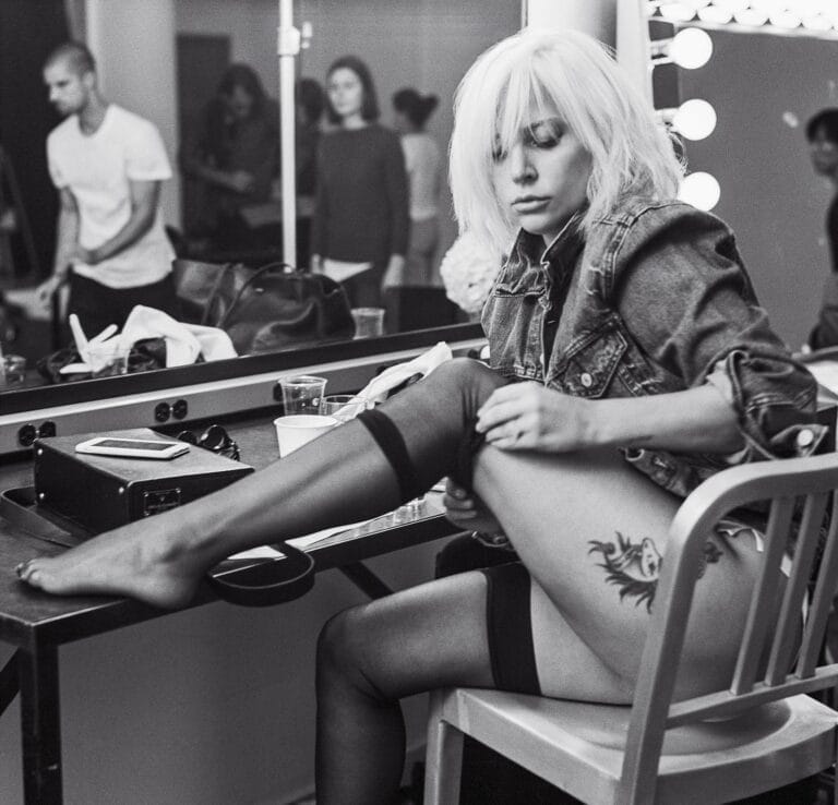Lady Gaga: Cabello rubio, chaqueta de mezclilla y medias negras. Está en lo que parece ser…