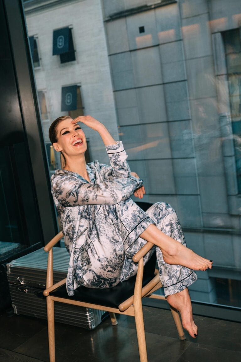 Rosamund Pike: Sentada en una silla moderna, con una gran sonrisa, lleva un conjunto de pijama…