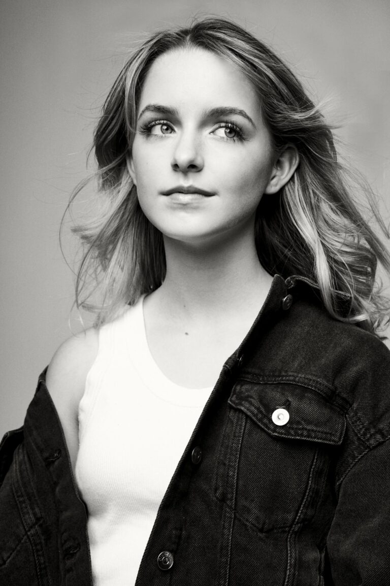Mckenna Grace: Sports a white sleeveless top and a dark denim jacket, partially unbuttoned.…